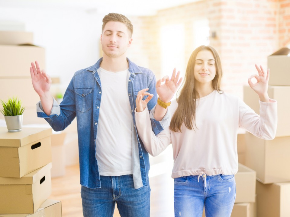 young couple moving to a new house relax and smiling with eyes closed doing meditation gesture with fingers