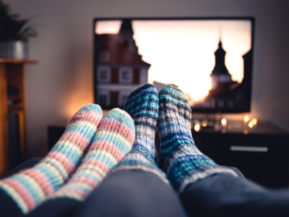 two people with their feet up in fluffy socks in front of a TV with fairy lights