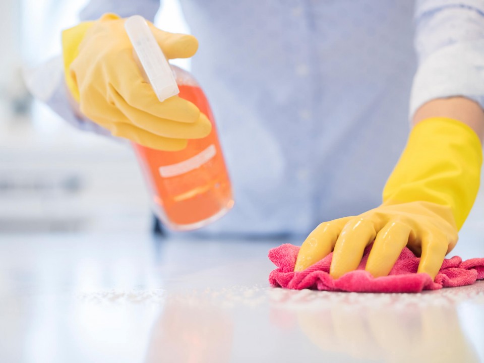 person cleaning a kitchen surface wearing yellow marigold gloves