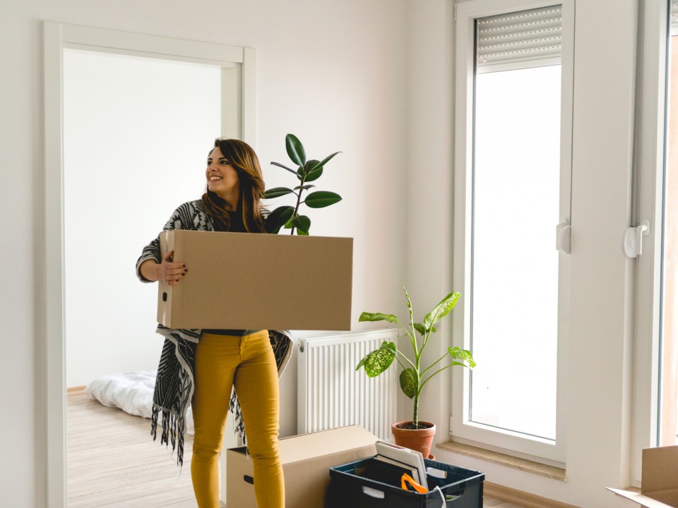 a woman smiling holding a cardboard box in an apartment